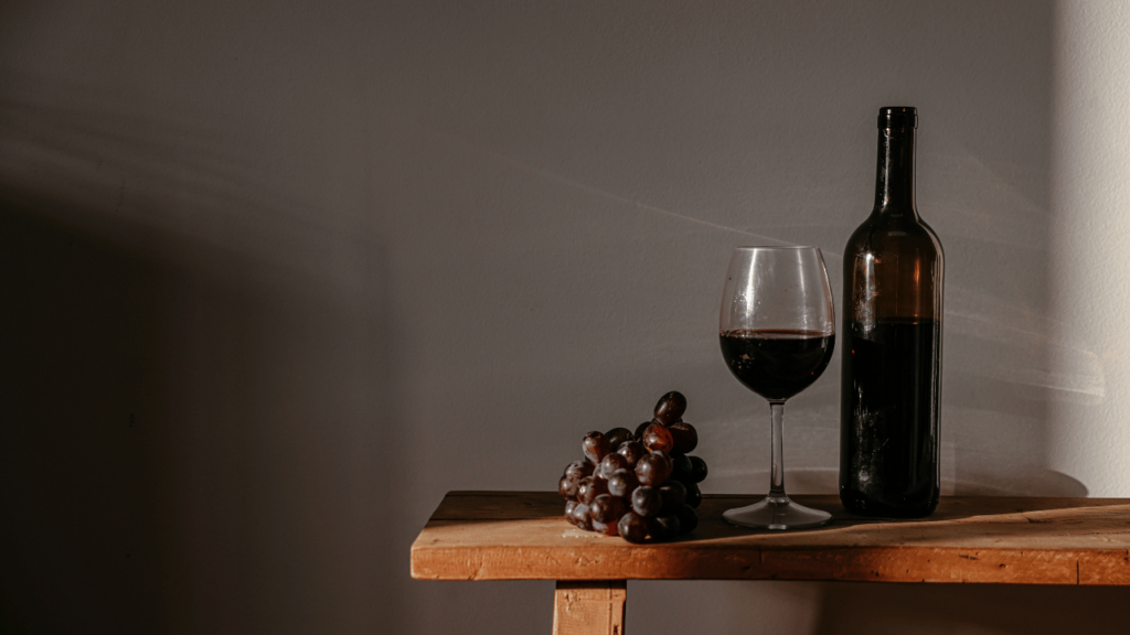 wood bench with bottle of red wine, glass of wine and red grapes